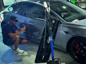 A Dents By Hand writing a dent estimate on a Tesla, Capturing a photo of the dent while using reflective lighting.